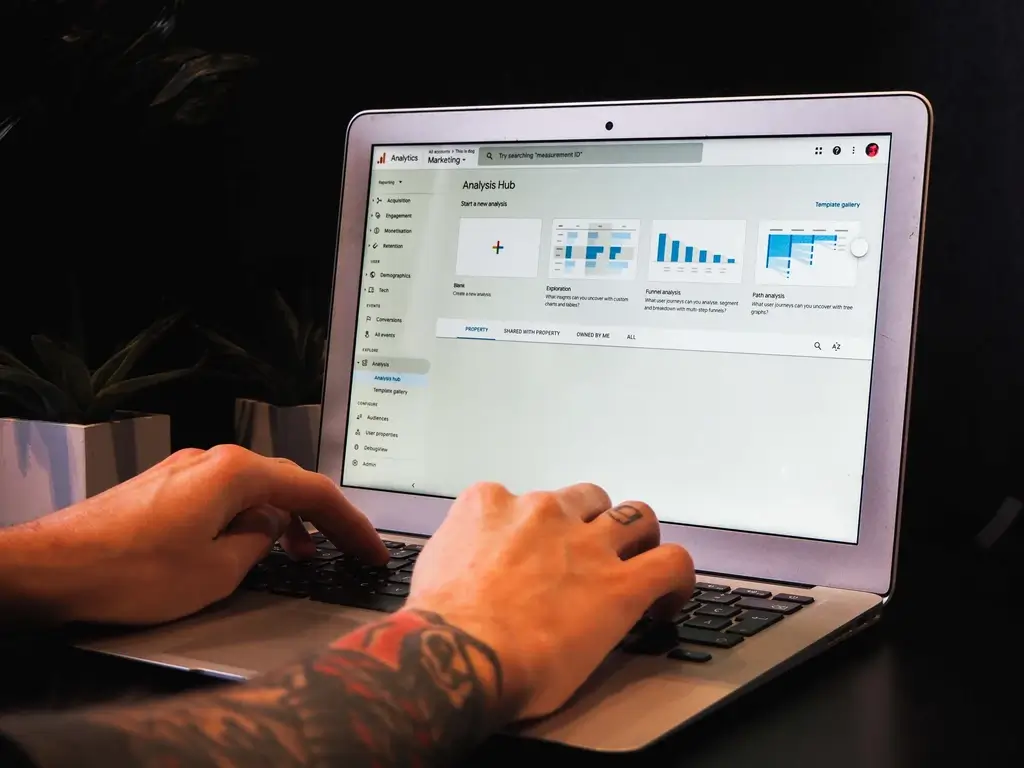 Man with tattoos on wrist using a laptop with the GA4 analysis hub displayed.