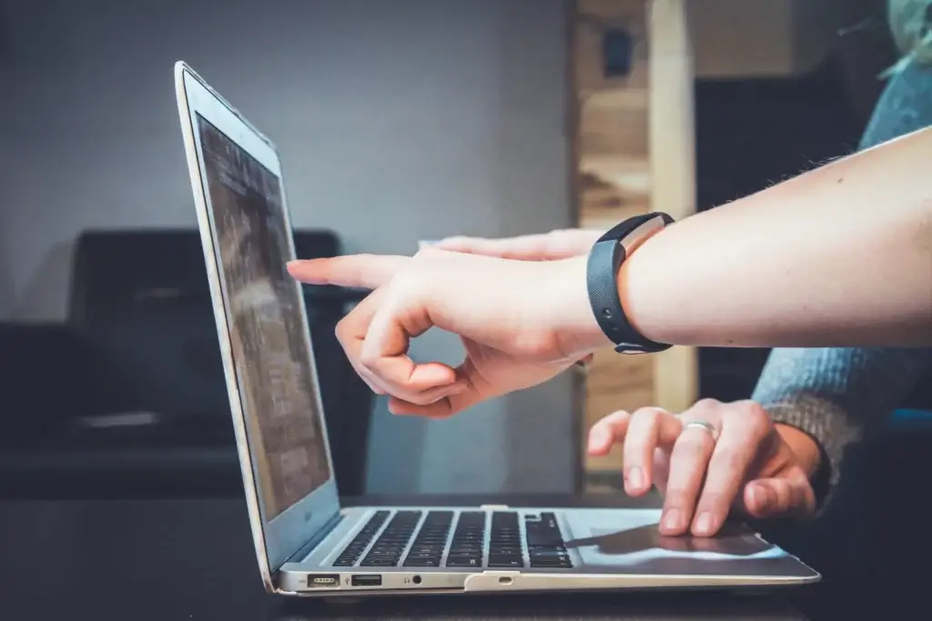 image of two people and a laptop, one is using the laptop's trackpad while the other is pointing at the screen